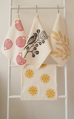 three tea towels hanging on a rack with oranges and pomegranates