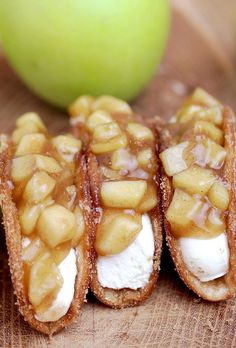 three pieces of food sitting on top of a wooden cutting board next to an apple