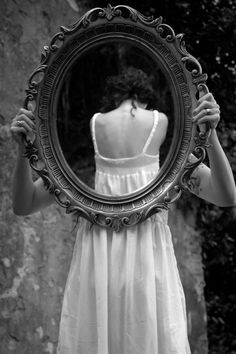 a woman in white dress holding up a mirror to look at her back and shoulder