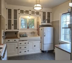 a kitchen with white cabinets and an old fashioned refrigerator freezer in the corner next to a window