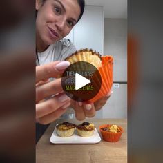 a woman is holding up a cupcake in front of some muffins