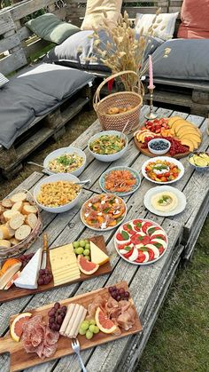 an outdoor picnic table filled with cheeses, meats and fruit platters on wooden boards