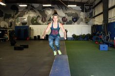 a woman is jumping on a trampoline in an indoor gym with camouflage walls