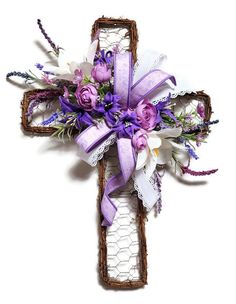 a cross decorated with purple flowers and white lace is displayed on a wall or table