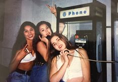 three women standing next to each other in front of a phone booth