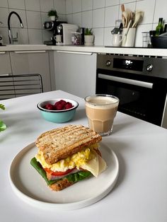 a white plate topped with a sandwich next to a bowl of strawberries and a cup of coffee