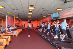 people are running on treadmills in an orange room with large screens above them