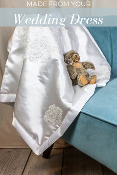 a teddy bear sitting on top of a blue couch under a white blanket with flowers