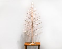 a small white christmas tree sitting on top of a wooden table next to a wall