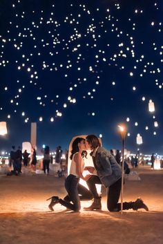 two people kneeling down to kiss in the middle of a field with lanterns flying overhead