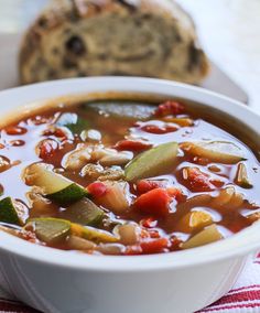 a white bowl filled with vegetable soup next to a loaf of bread