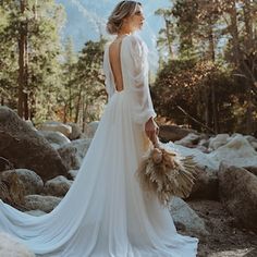 a woman in a white wedding dress standing on rocks with her back to the camera