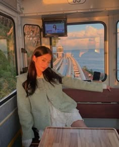 a woman sitting at a table on a train looking out the window with her arm outstretched