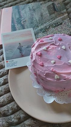 a pink frosted cake sitting on top of a white plate next to a book