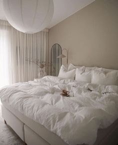 a bed with white linens and pillows in a bedroom next to a large window