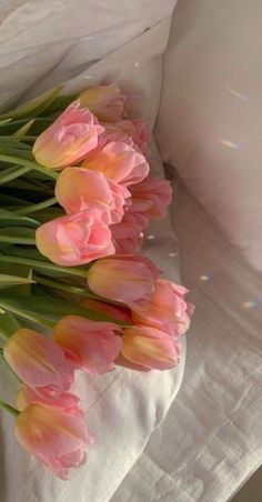 a bunch of pink tulips are laying on a white bed sheet with sunlight shining in the background