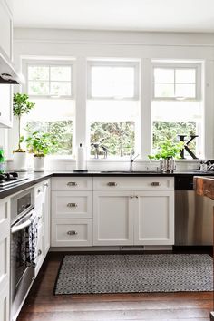 a kitchen with white cabinets and stainless steel appliances, along with potted plants in the window sill