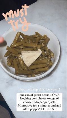 a bowl filled with green beans and cheese on top of a white marble countertop