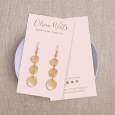 two gold earrings on top of a card next to a plate with a pair of earring