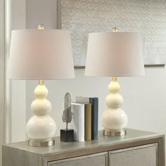 two white lamps sitting on top of a table next to a book and lamp shade