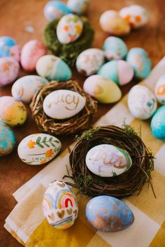 painted eggs sitting on top of a checkered table cloth next to a bird's nest