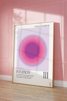 a pink and purple poster on the floor in front of a pink wall with a wooden frame