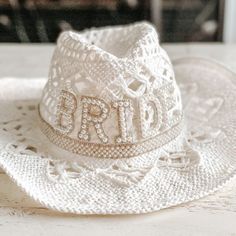 a white hat with the word bride written on it sitting on a doily covered table