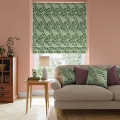 a living room with pink walls and green patterned roman shades on the window sill