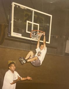 two men are playing basketball in an indoor court while one man is jumping up to the basket