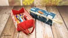 an open pencil case sitting on top of a wooden table next to a bag with pens and pencils in it