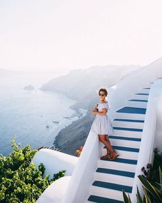 a woman standing at the top of a staircase next to an ocean and mountains area