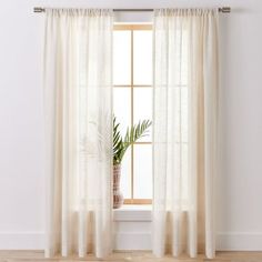 a window with curtains and a potted plant on the ledge in front of it