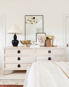 a white dresser with two lamps and pictures on top of it in a living room