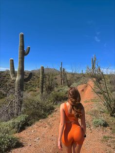 a woman in an orange swimsuit walking down a dirt road next to a cactus