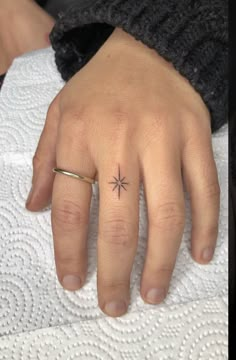 a woman's hand with a small star tattoo on her left thumb and ring