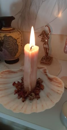 a lit candle sitting on top of a shell next to a vase and figurine