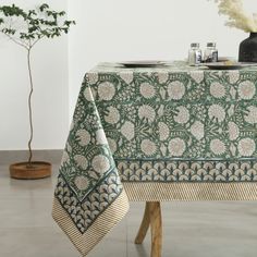 a green table cloth with white flowers on it and a black vase in the background