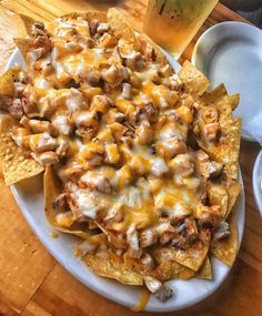 a white plate topped with nachos covered in cheese and sauce next to a glass of beer