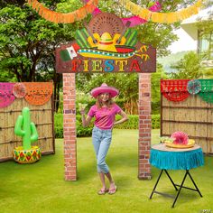 a woman wearing a sombrero standing in front of a mexican fiesta sign and decorations