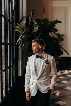 a man in a tuxedo standing next to a window