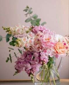 a vase filled with pink and white flowers sitting on top of a wooden table next to a mirror