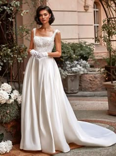 a woman in a wedding dress standing on the ground next to some white flowers and greenery