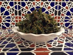 a white bowl filled with green vegetables on top of a tiled counter next to a blue and red tile wall