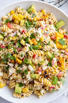 a white bowl filled with pasta salad and topped with avocado, tomatoes, corn, cilantro