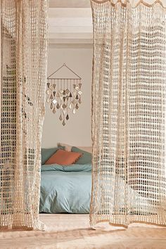 a bed sitting next to a window covered in sheer curtains and hanging chandelier