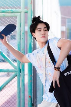 a young man holding a ping pong paddle in his right hand while standing next to a fence