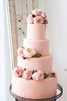 a three tiered cake with pink frosting and flowers on top is sitting on a table