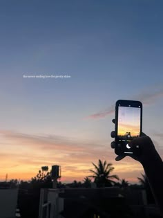 someone holding up their cell phone to take a photo with the sunset in the background