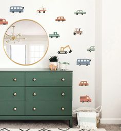 a green dresser sitting next to a wall with cars on it and a round mirror