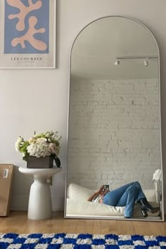 a person laying on a bed in front of a large mirror with a blue and white rug